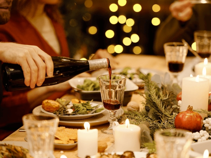 hand pooring red wine into glass at dinner table