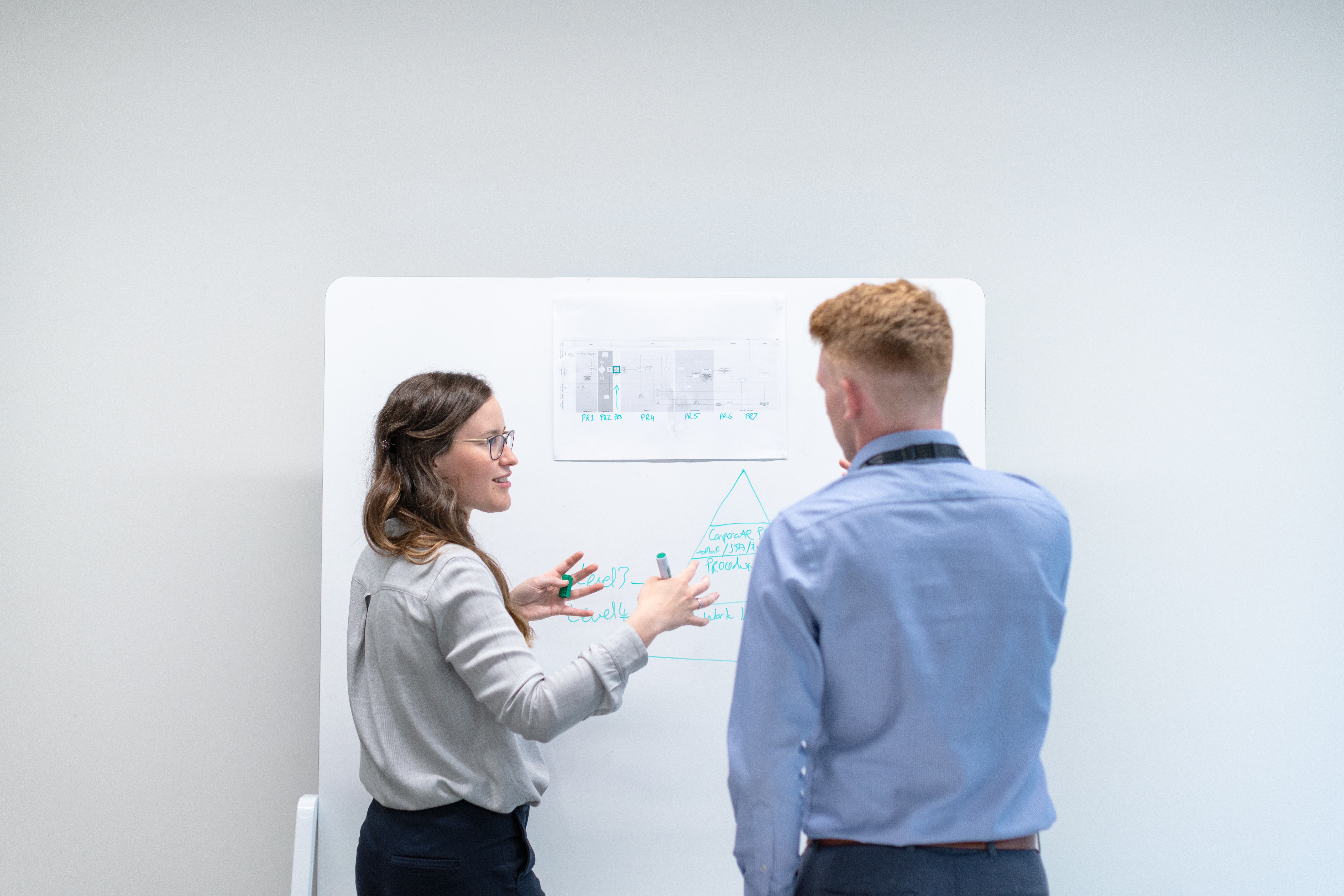 two people standing in front of a white board